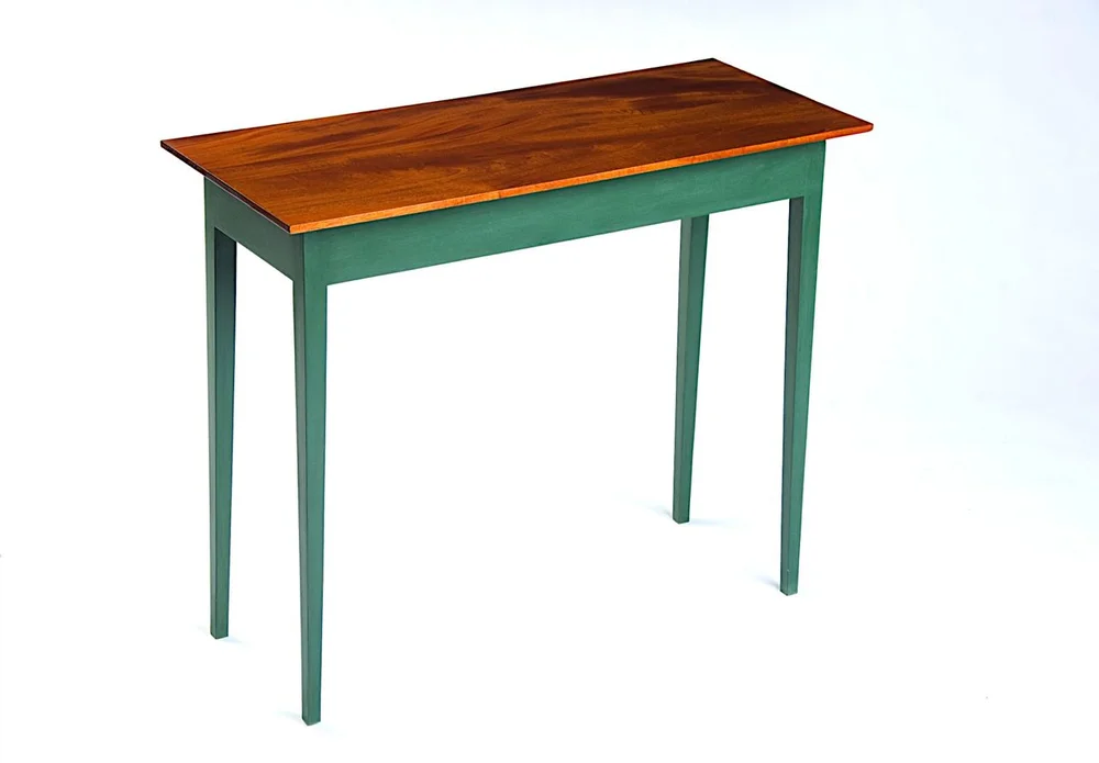 A small rectangular wooden side table with a warm brown wood-grain top and green painted tapered legs, shown against a plain pale wall